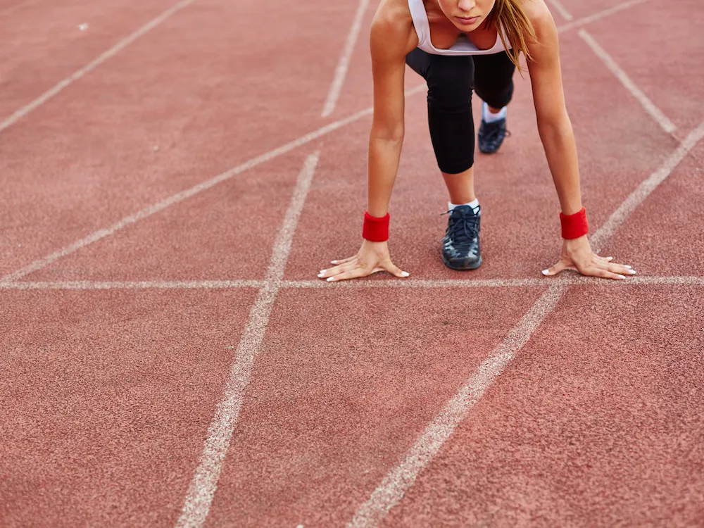 A woman on a running track set in starting position.