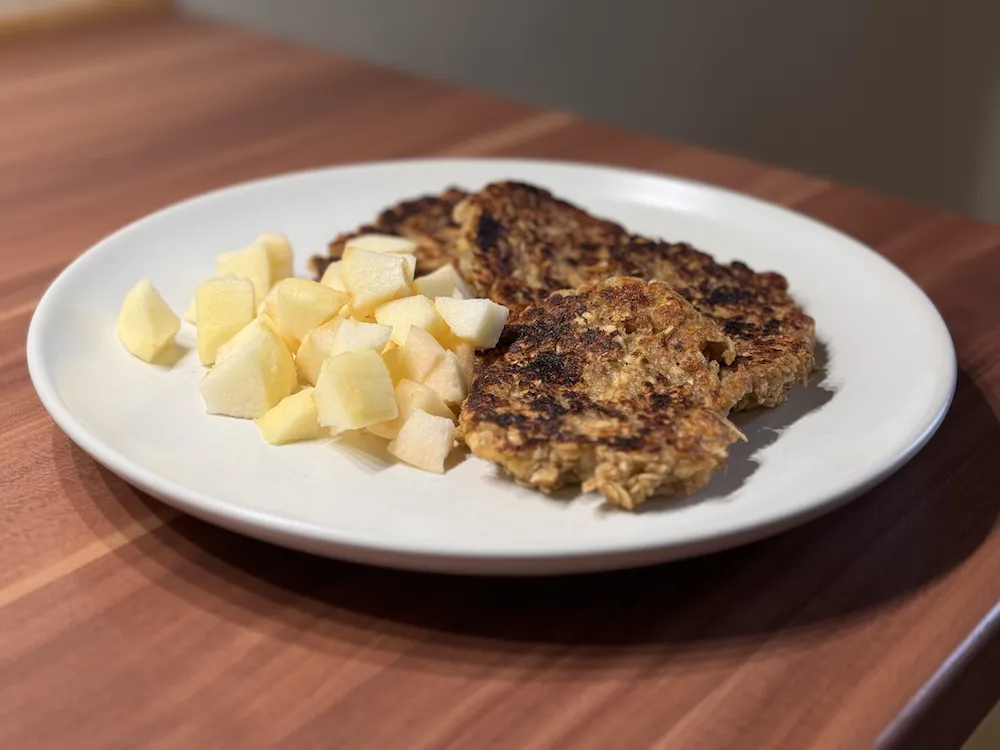 Banana and oat pancakes with fresh apple pieces on the side.